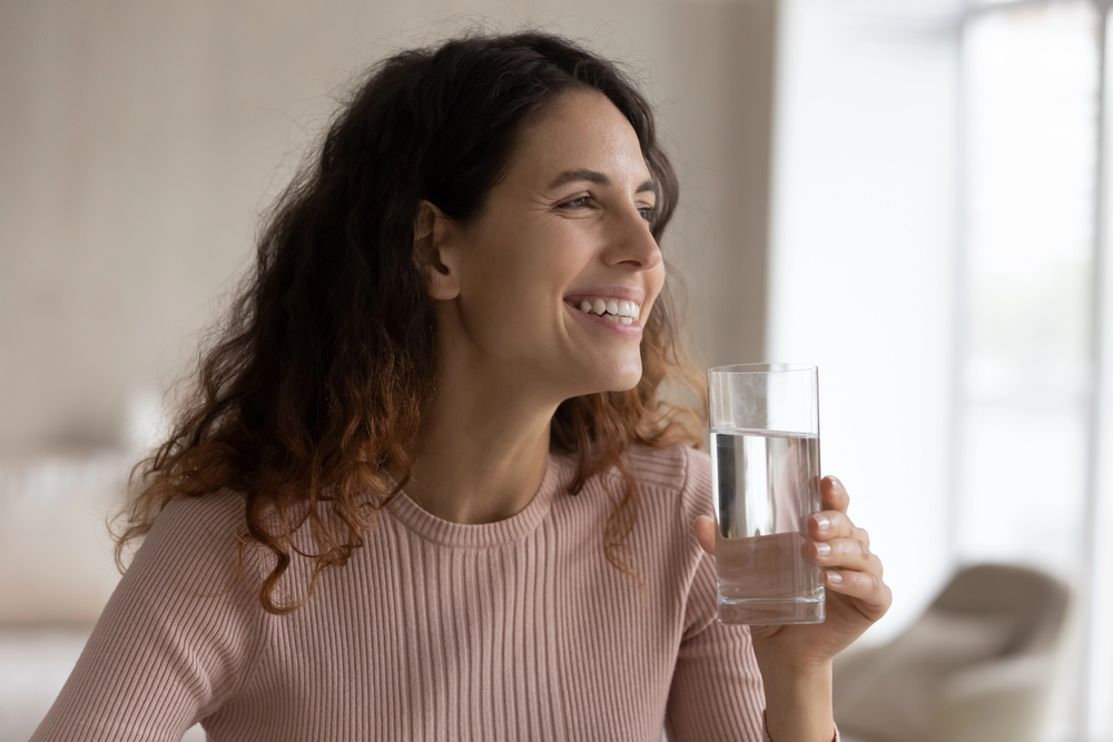 A woman holding a clean glass of water, showing the effects of choosing the right water softener.