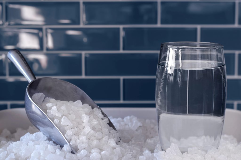 Water softener next to a glass of clean water demonstrating the importance of a Houston homeowner’s settings.